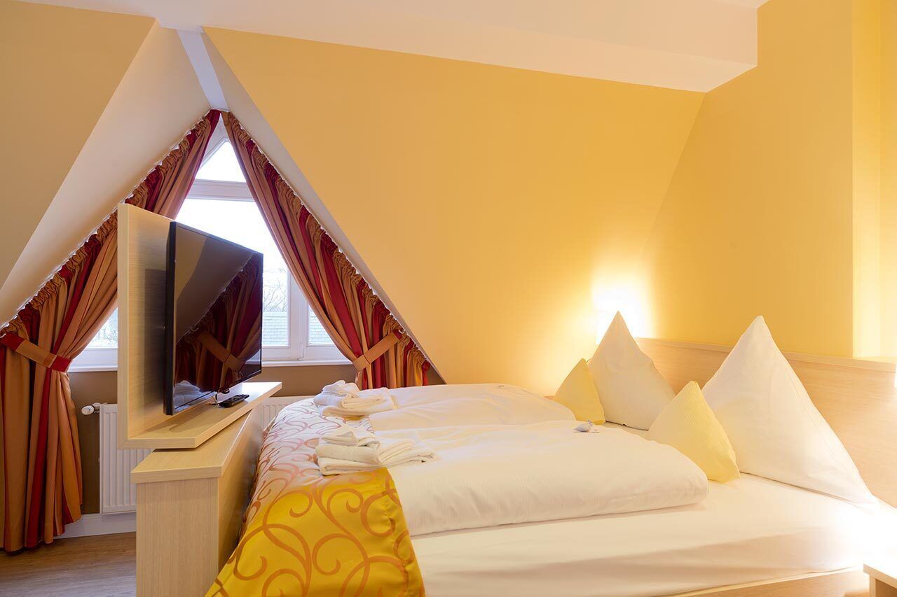 Una habitación de hotel con cama, televisión y ventana con cortinas.