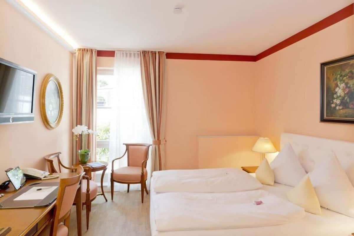A hotel room with a bed, desk, chair, and a TV.