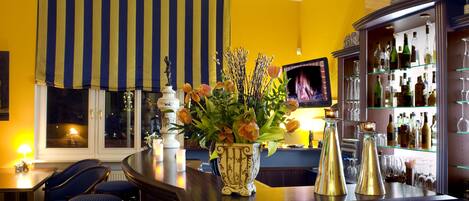 Un espace bar comprenant un comptoir, des tabourets de bar, un vase décoratif avec des fleurs et une étagère avec des bouteilles et des verres.