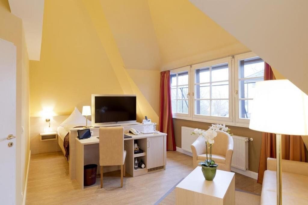 Hotellihuone, jossa on sänky, työpöytä, televisio ja ikkuna, jossa on verhot.
