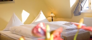 A hotel room with a bed, pillows, a lamp, and a window with curtains.