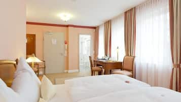 Une chambre d’hôtel avec un lit, un bureau et une chaise. Il y a une porte qui donne sur une autre pièce et une fenêtre avec des rideaux.