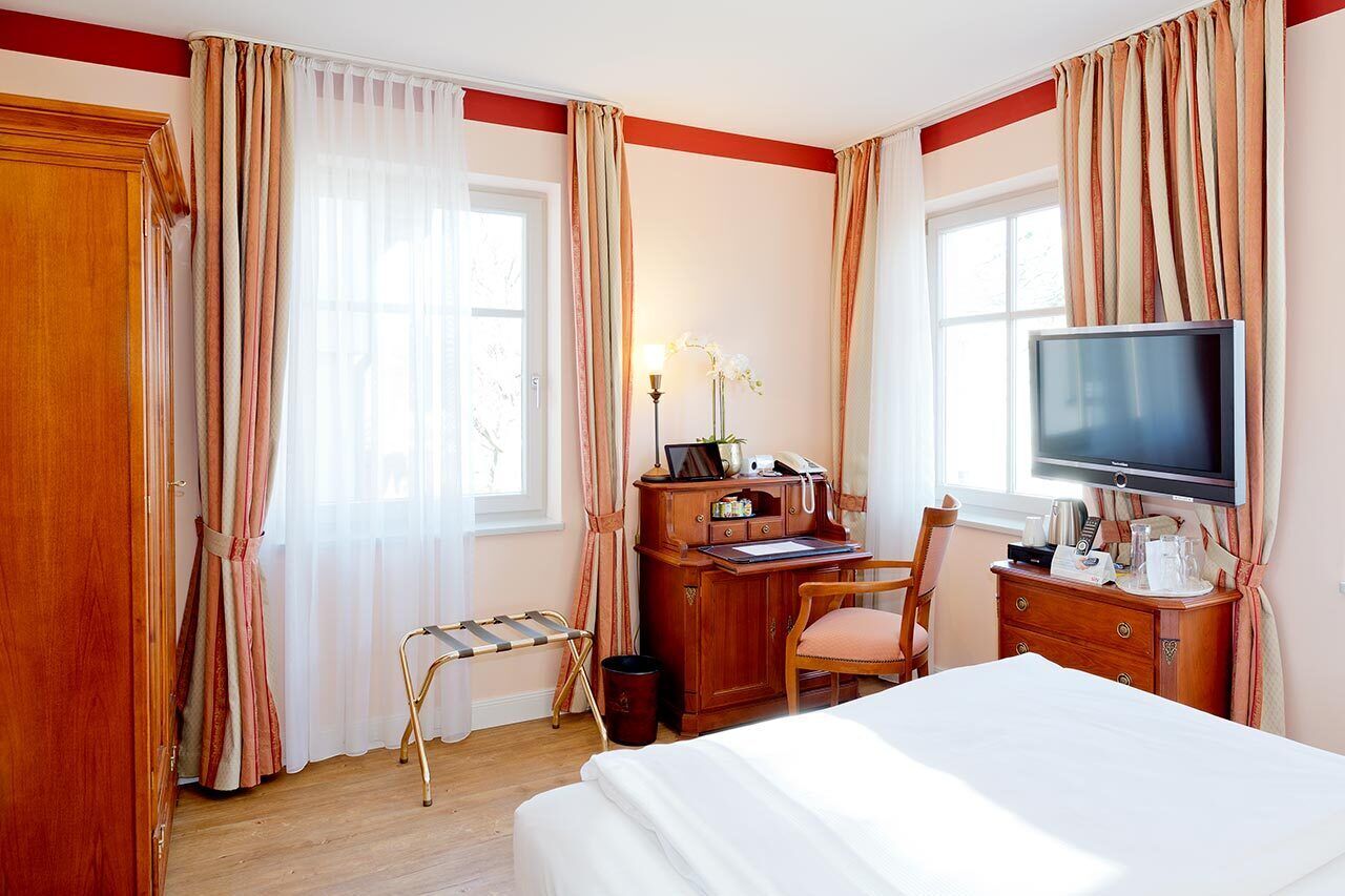 A hotel room with a bed, a desk with a chair, a television, and a window with curtains.