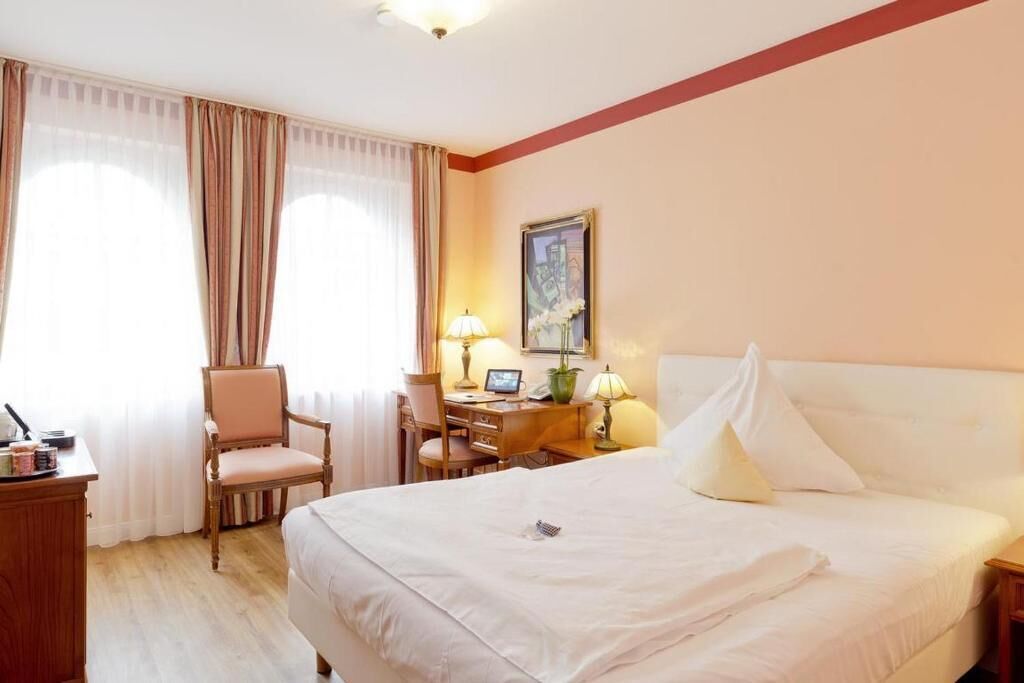 Una habitación de hotel con cama, escritorio, silla y cortinas.