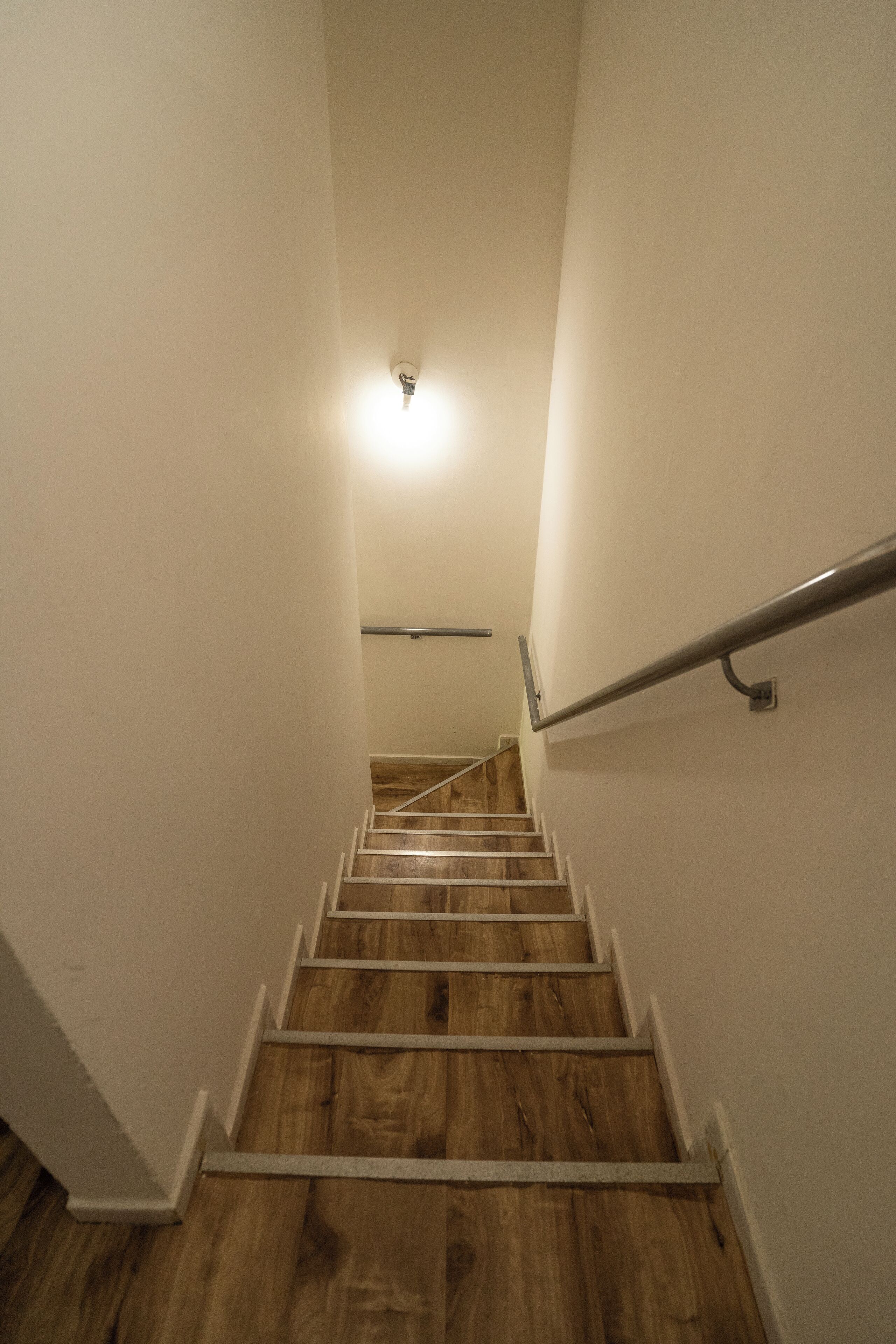 Una escalera de madera con paredes blancas que conduce a una plataforma con una lámpara.