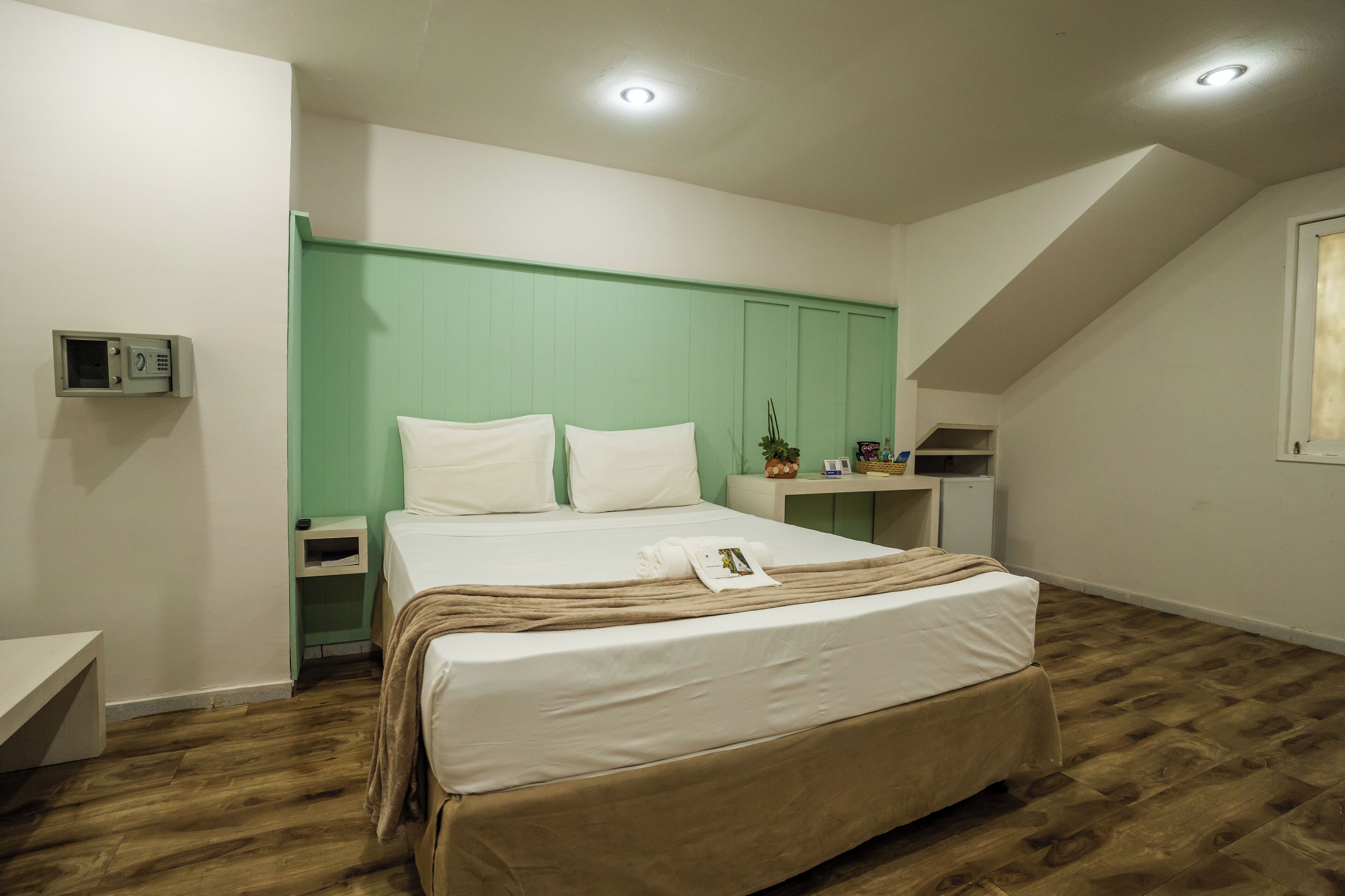 A bedroom with a bed, bedside tables, a green headboard, a small shelf with items, and a window.