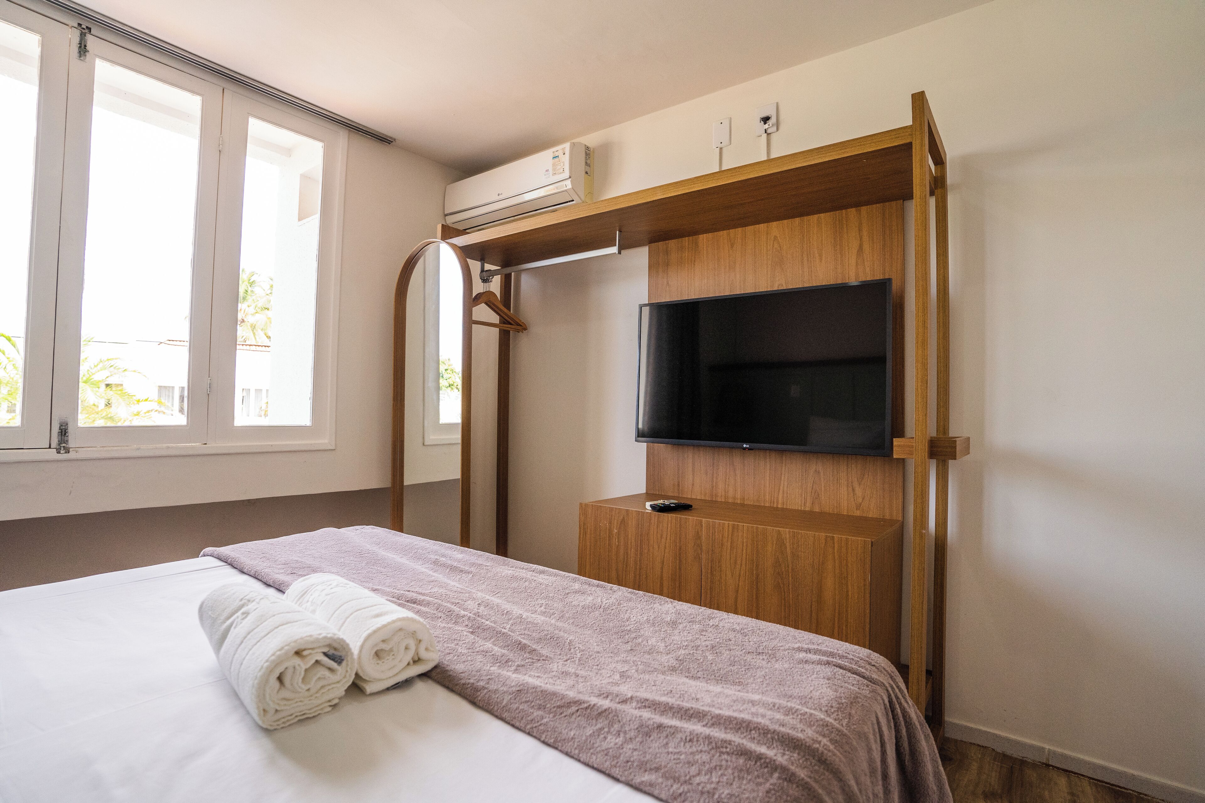 Habitación de hotel con cama, televisor montado en un estante de madera y unidad de aire acondicionado encima del estante.