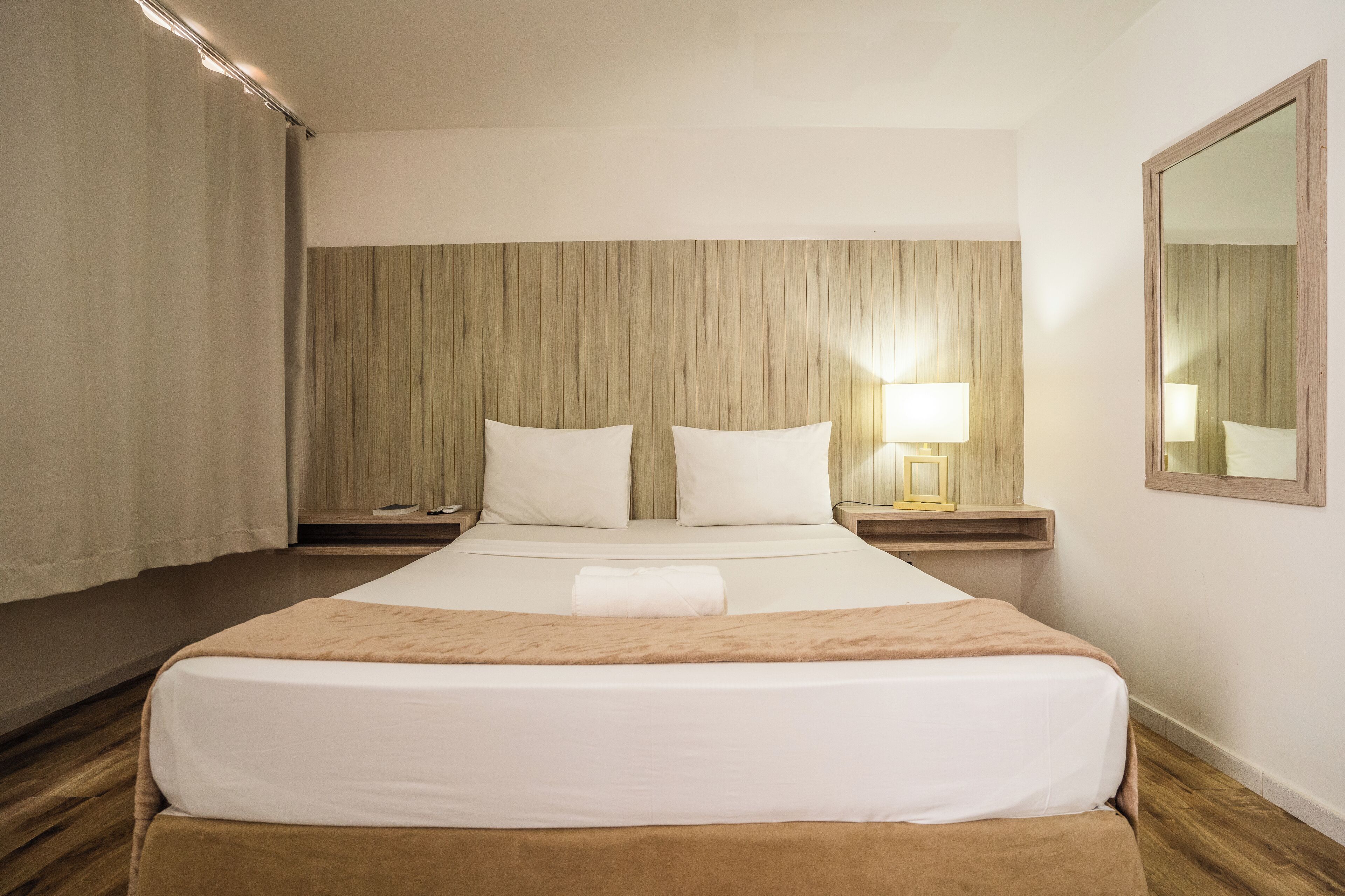 A hotel room with a large bed, wooden headboard, bedside lamps, and a mirror on the wall.