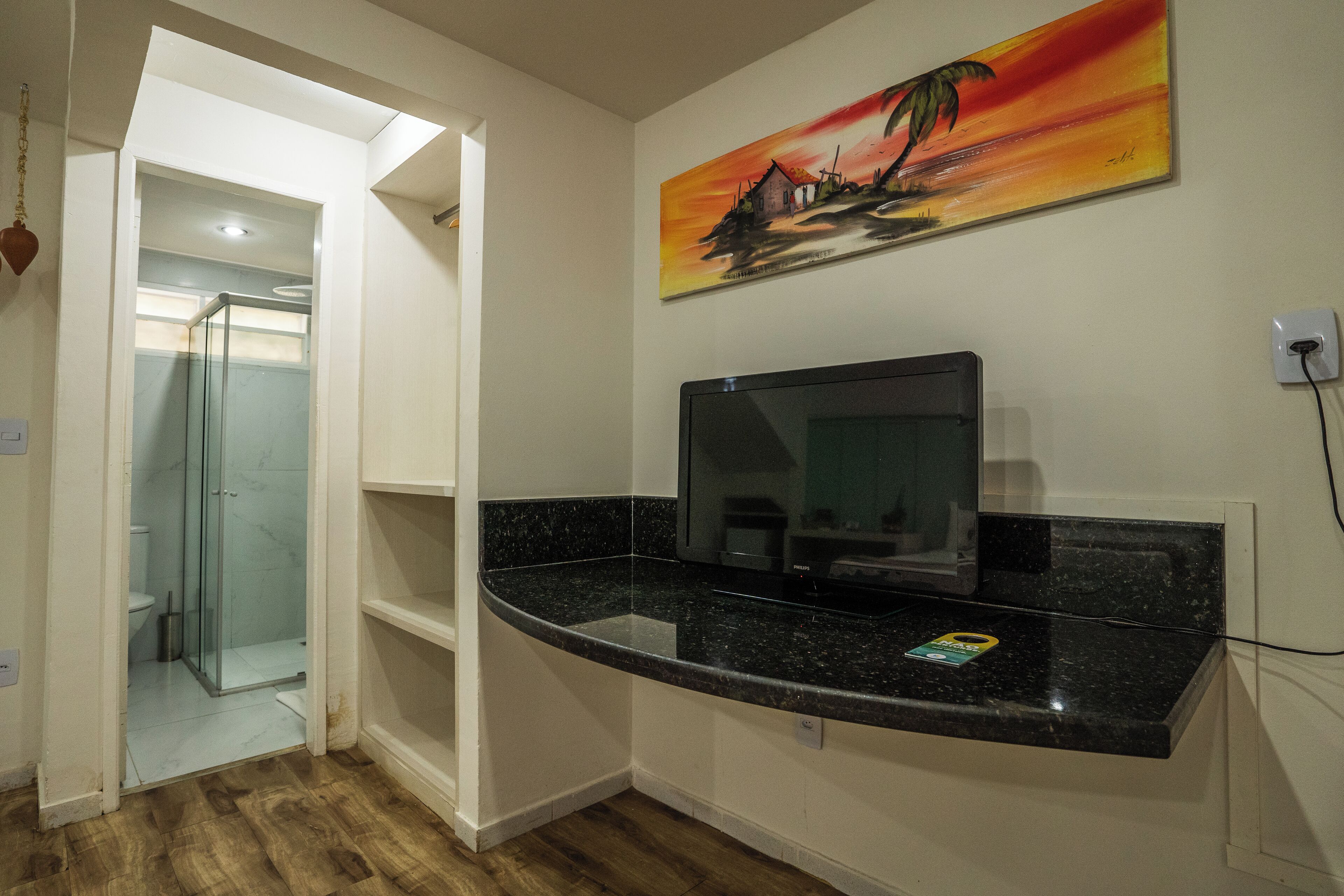 A bathroom with a glass shower enclosure, a black countertop, and a painting of a sunset scene.