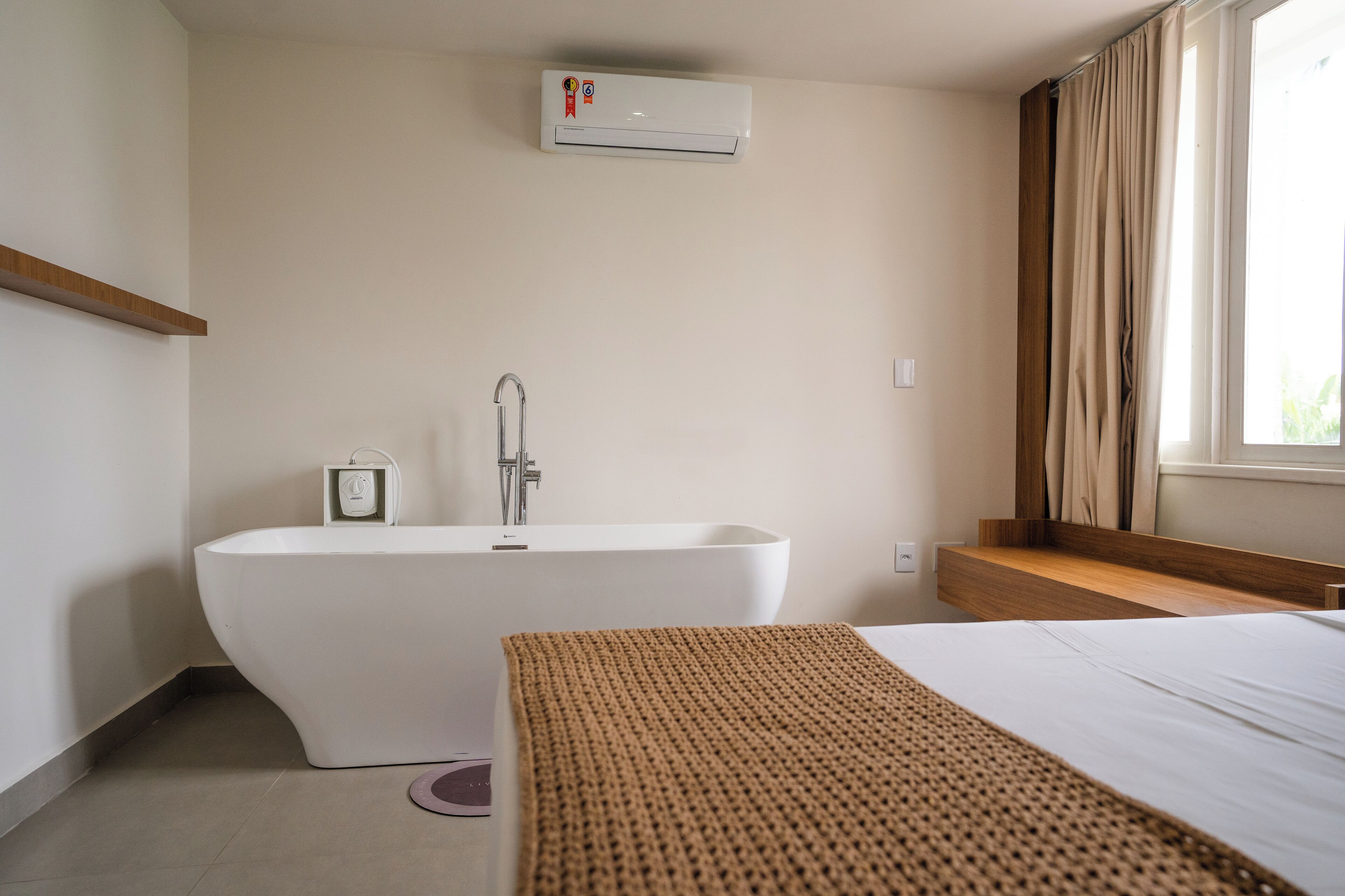 Un baño moderno con una bañera independiente, un perchero y un ventanal con cortinas.