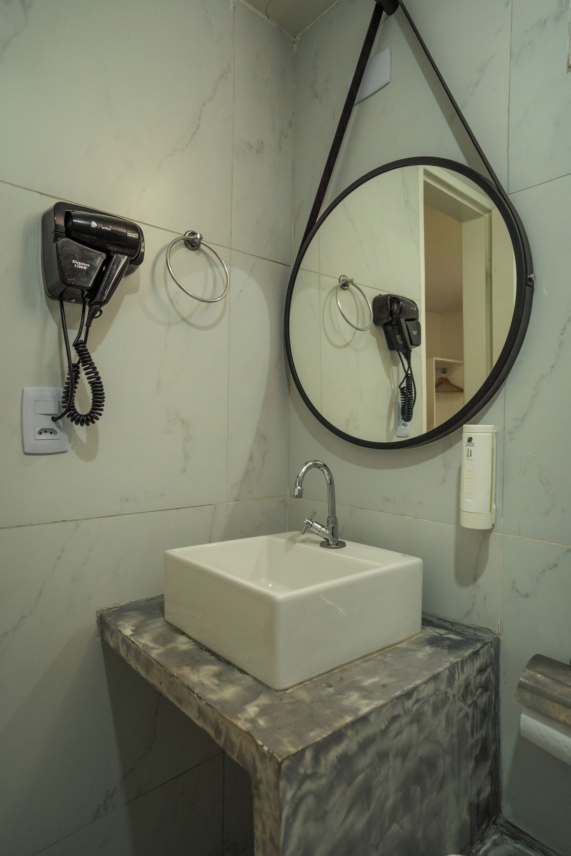 Un baño con lavamanos de mármol, un espejo redondo y un secador de pelo montado en la pared.