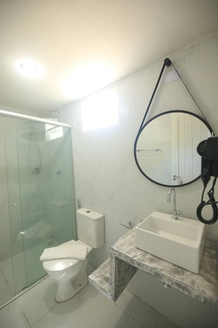 A bathroom with a glass-enclosed shower, a toilet, a sink with a marble countertop, and a round mirror with a black frame.