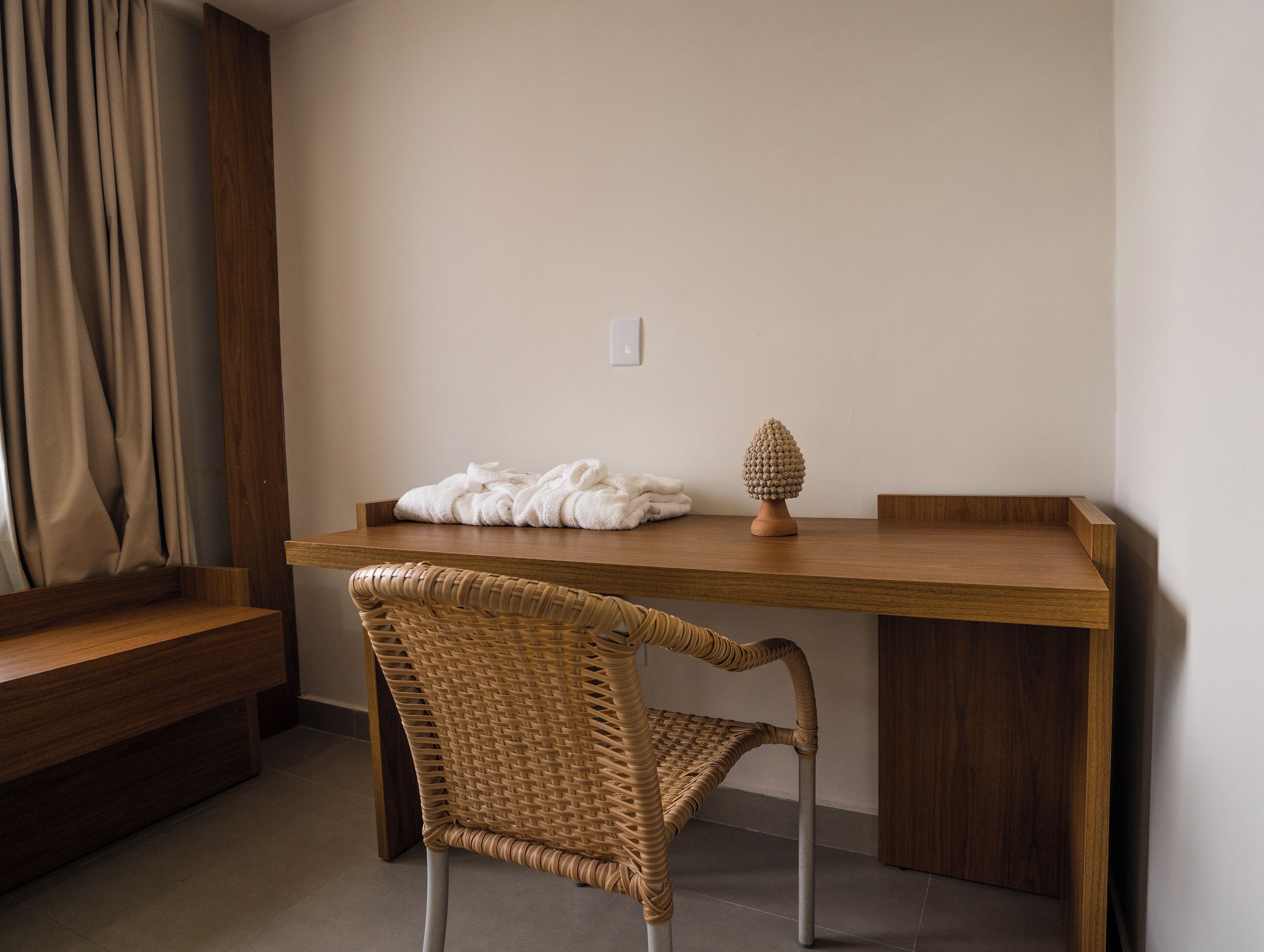 A room with a wooden desk, a wicker chair, a white towel, and a decorative object on the desk.