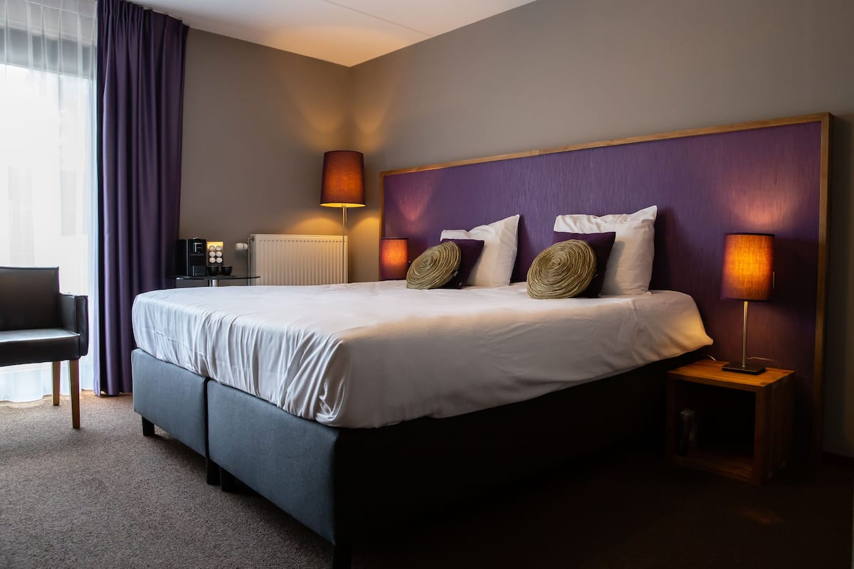 A hotel room with a large bed, two bedside lamps, a coffee maker, and a chair.