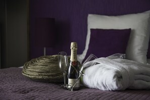 Un lit recouvert d’une couverture violette, une serviette blanche pliée, une bouteille de champagne Moët & Chandon et un verre posé sur une surface texturée.