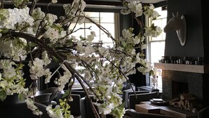 A room with a large artificial tree branch with white flowers, a stone fireplace, and modern furniture. - Linge Hotel Elst (Elst)
