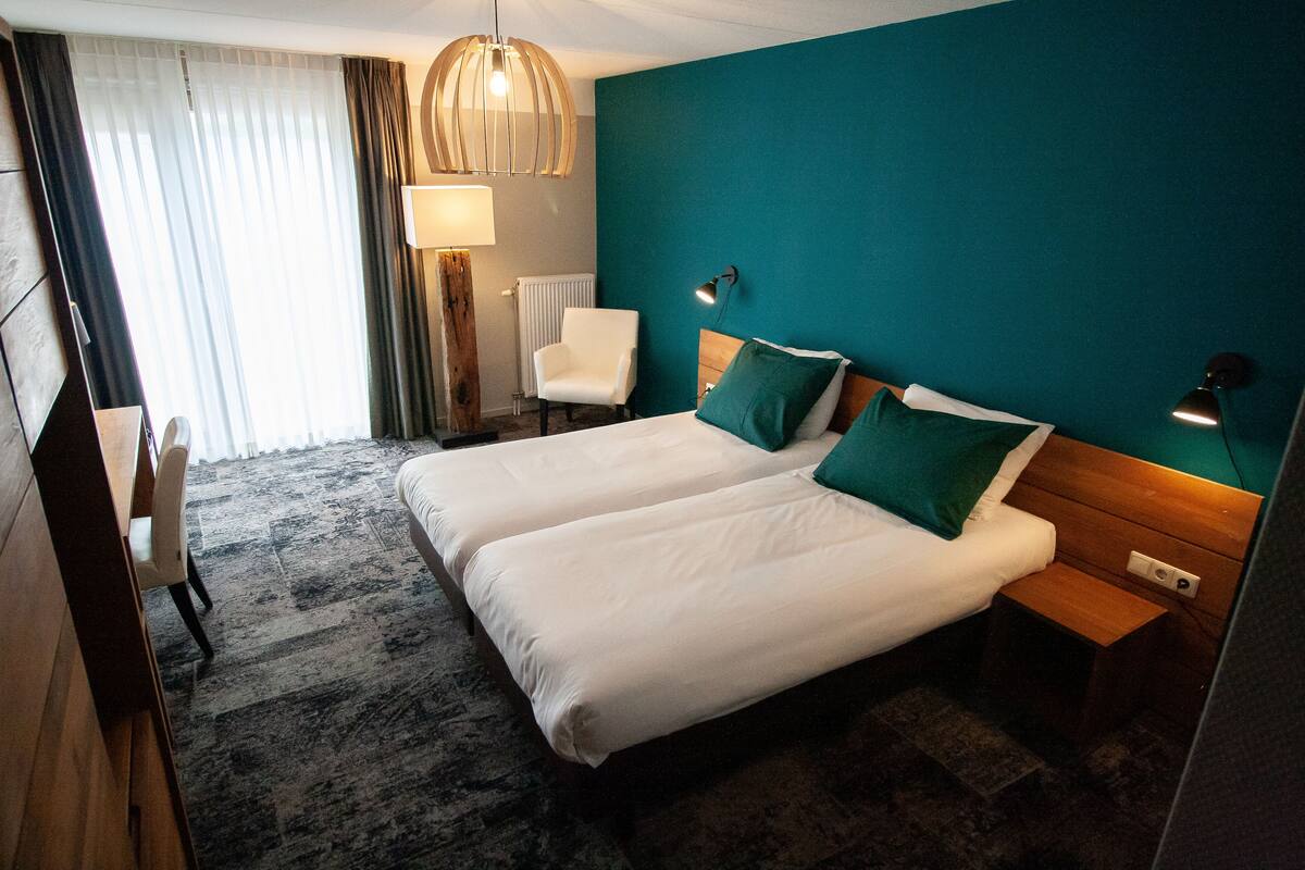 A hotel room with a large bed, two bedside tables, a chair, a desk, and a window with curtains.