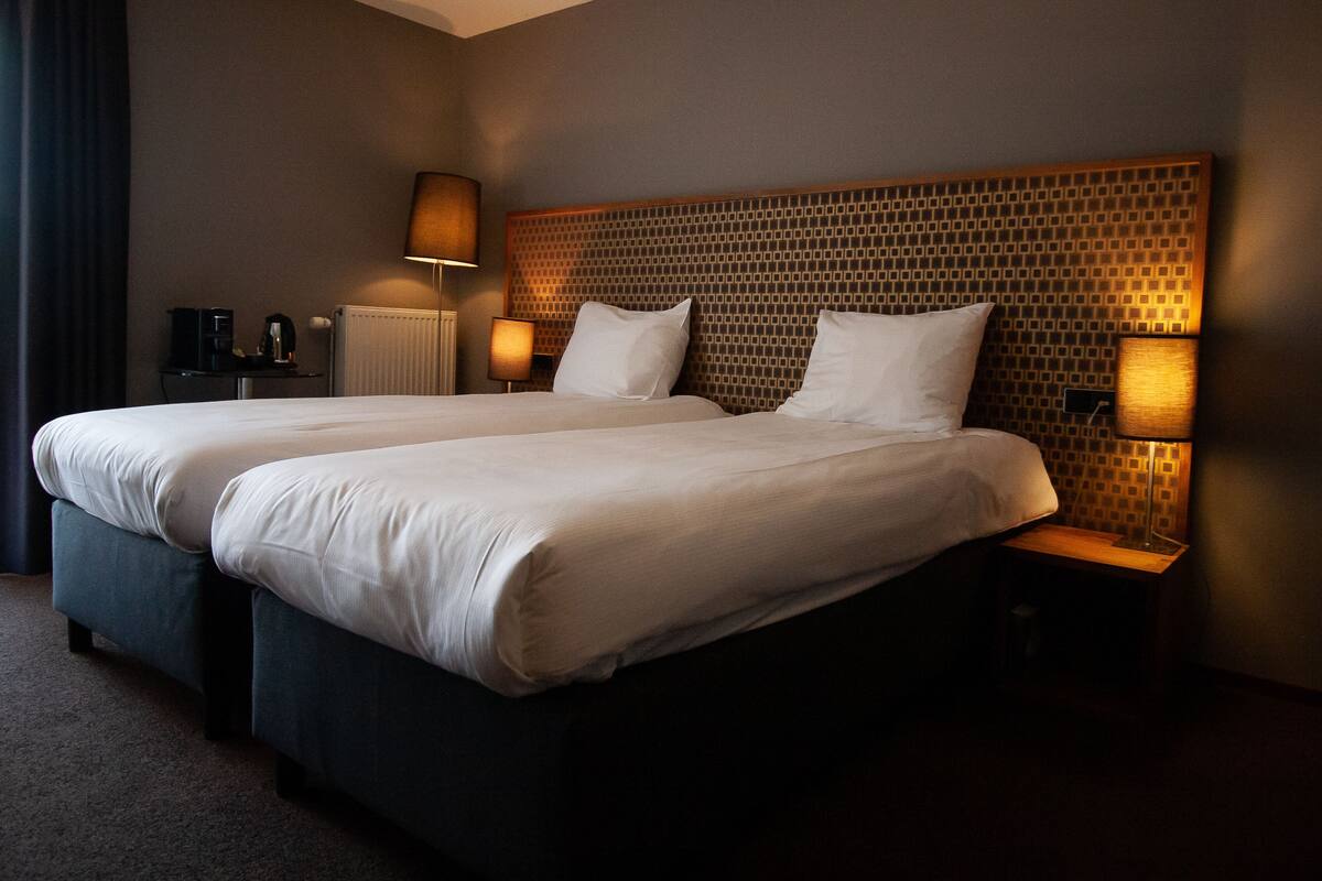 A double bed with a headboard featuring a geometric pattern, two bedside tables with lamps, and a radiator on the wall.
