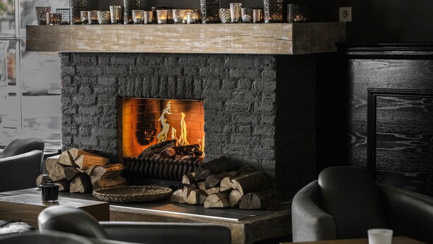 A stone fireplace with a fire, surrounded by seating and a coffee table. - Linge Hotel Elst (Elst)