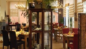 A dining area with multiple tables and chairs, a central decorative piece, and large windows with curtains.