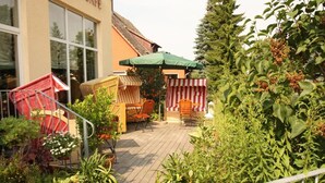 A patio area with outdoor furniture, a striped awning, and lush greenery.