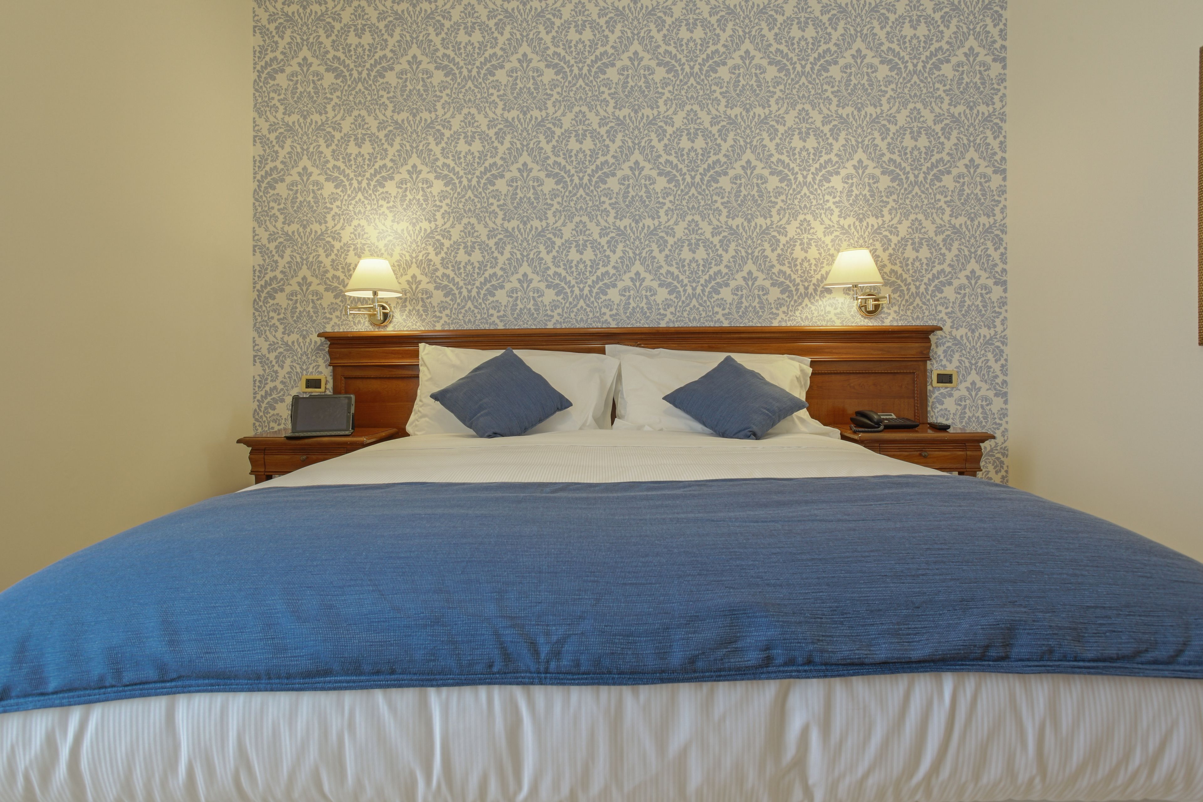 A neatly made bed with a blue bedspread and pillows, two bedside lamps, and a nightstand with a phone.