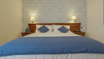 A neatly made bed with a blue bedspread and pillows, two bedside lamps, and a nightstand with a phone.
