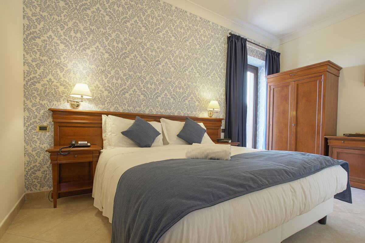 A neatly made bed with a wooden headboard, two bedside tables with lamps, and a wardrobe.