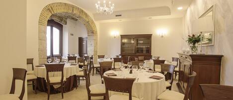 A dining area with round tables, wooden chairs, and a chandelier.