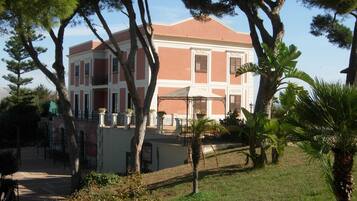 Un edificio de dos pisos con fachada roja y blanca, rodeado de árboles y césped.