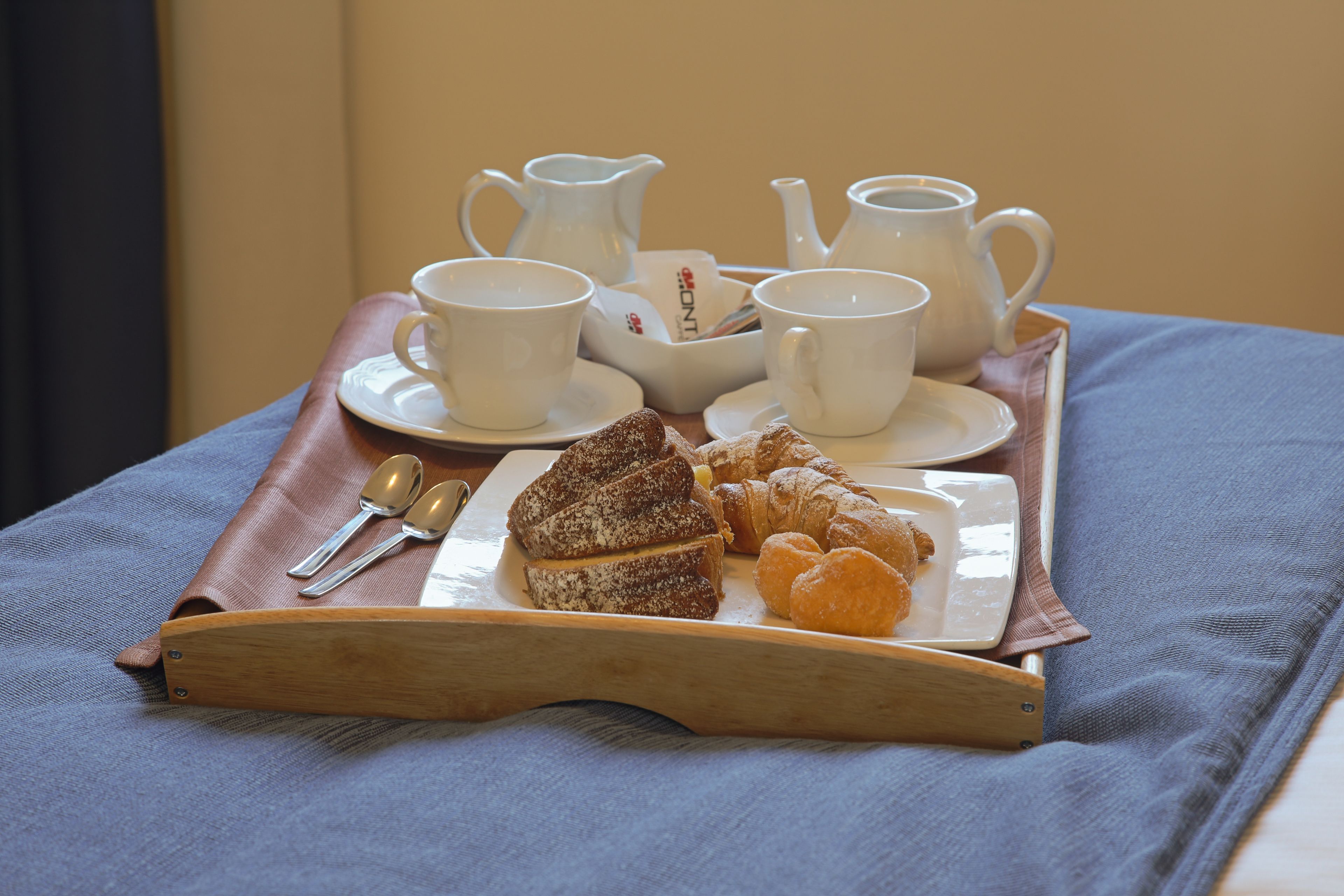 A tray with a coffee set, croissants, and pastries on a bed.