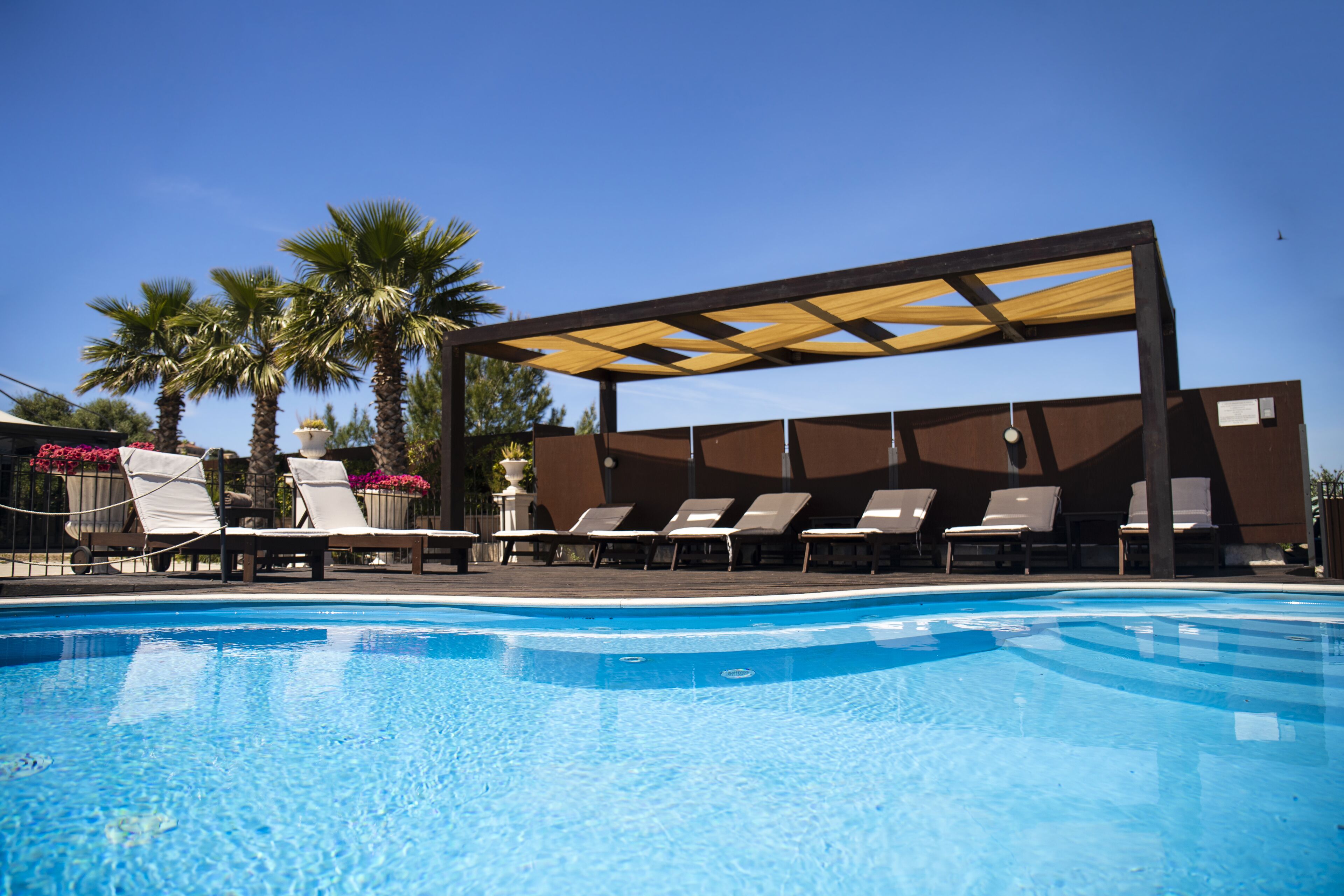 Una piscina con lettini da sole e una zona all'ombra.