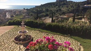 A courtyard with a fountain, potted flowers, and a view of a coastal town and hilltop castle. - Villa Giuliana Relais (Licata)