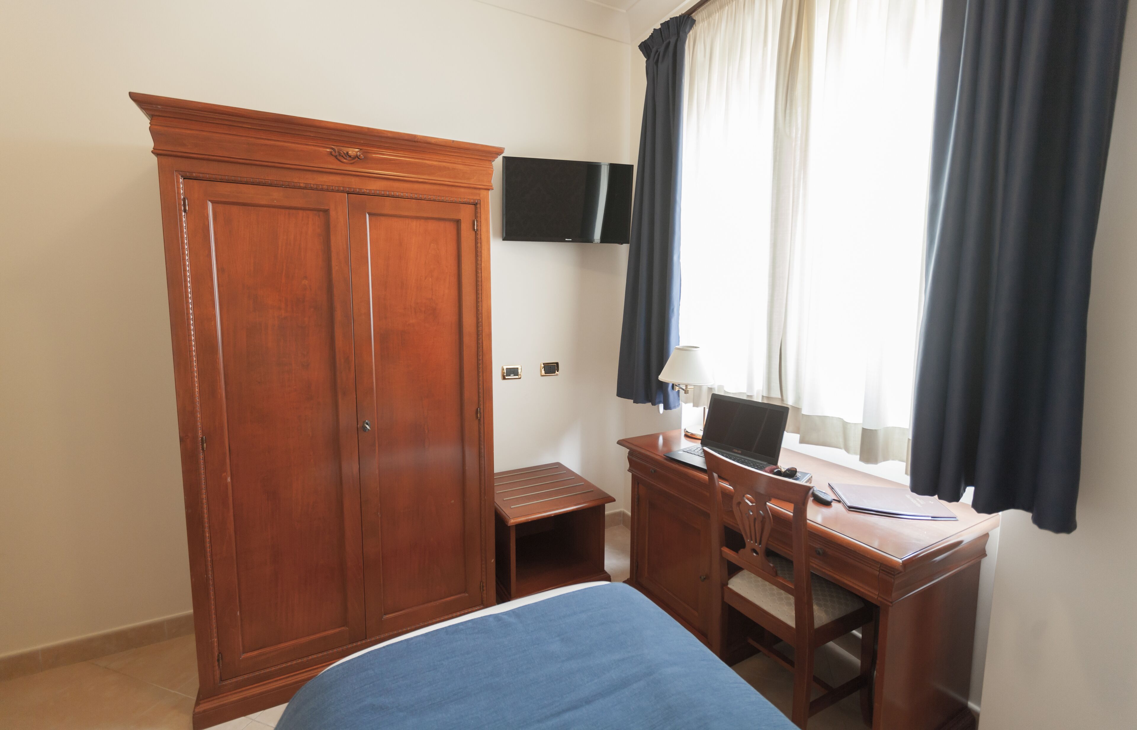 A room with a bed, a desk with a laptop, a television, and a wardrobe.