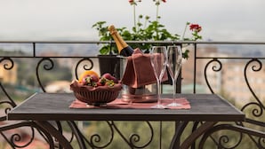 A table with a bottle of champagne, two glasses, and a bowl of fruit on a balcony with a view of buildings and flowers. - Villa Giuliana Relais (Licata)