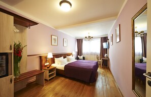 A hotel room with a bed, bedside tables, a TV, a mirror, and a wooden floor.