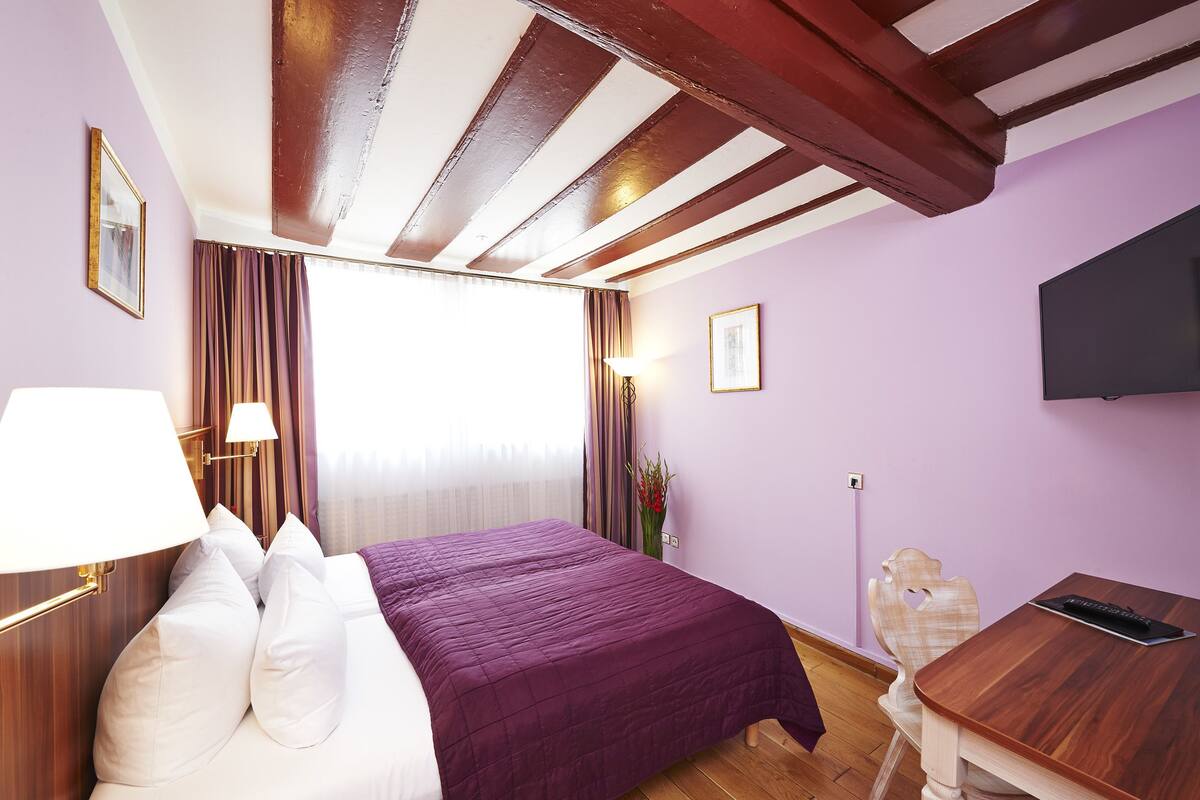 A hotel room with a bed, a desk, a TV, and a window with curtains.