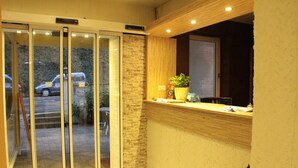 A reception area with a wooden counter, a potted plant, and a sliding glass door leading to an outdoor area. - Hotel Holl (Cochem)