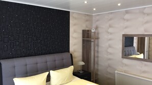 A modern bedroom with a large bed, a dark patterned wall, a wooden wardrobe, and a mirror. - Hotel Holl (Cochem)