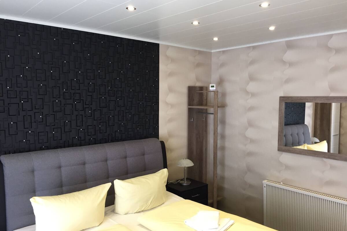 Ein modernes Schlafzimmer mit einem großen Bett, einer Wand mit dunklem Muster, einem Holzschrank und einem Spiegel.