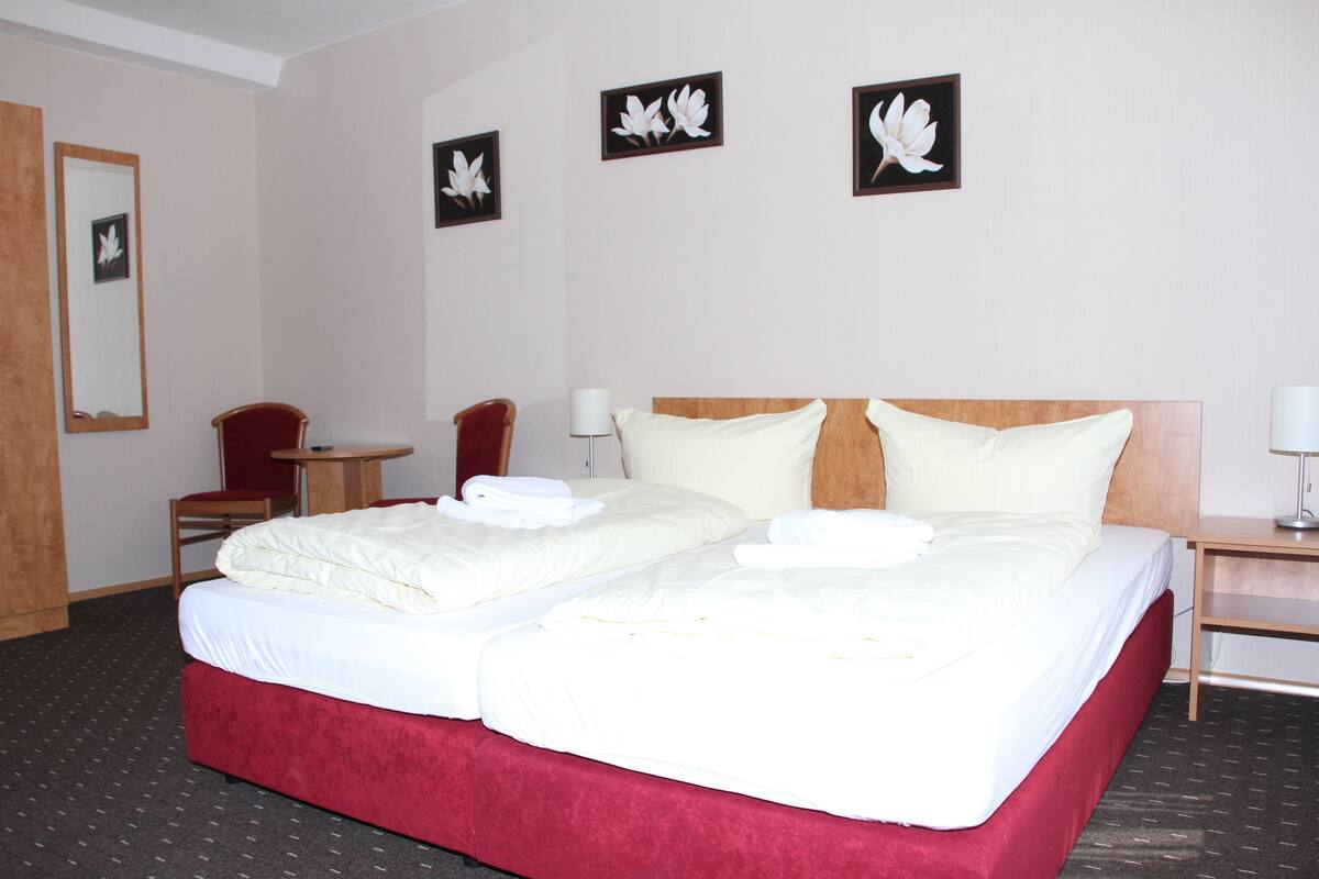 Ein Hotelzimmer mit einem großen Bett, zwei Stühlen, einem kleinen Tisch und drei an der Wand befestigten Blumenbildern.