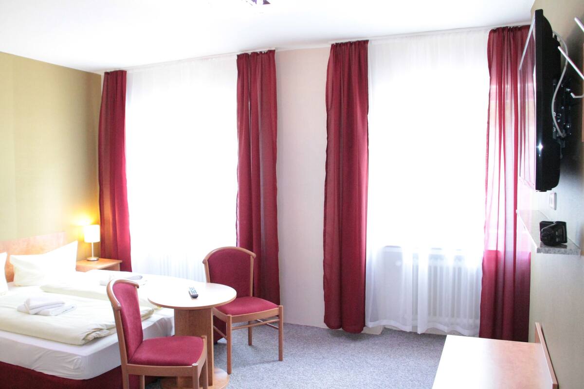 Ein Hotelzimmer mit Bett, zwei Stühlen, einem kleinen Tisch und einem Fernseher.