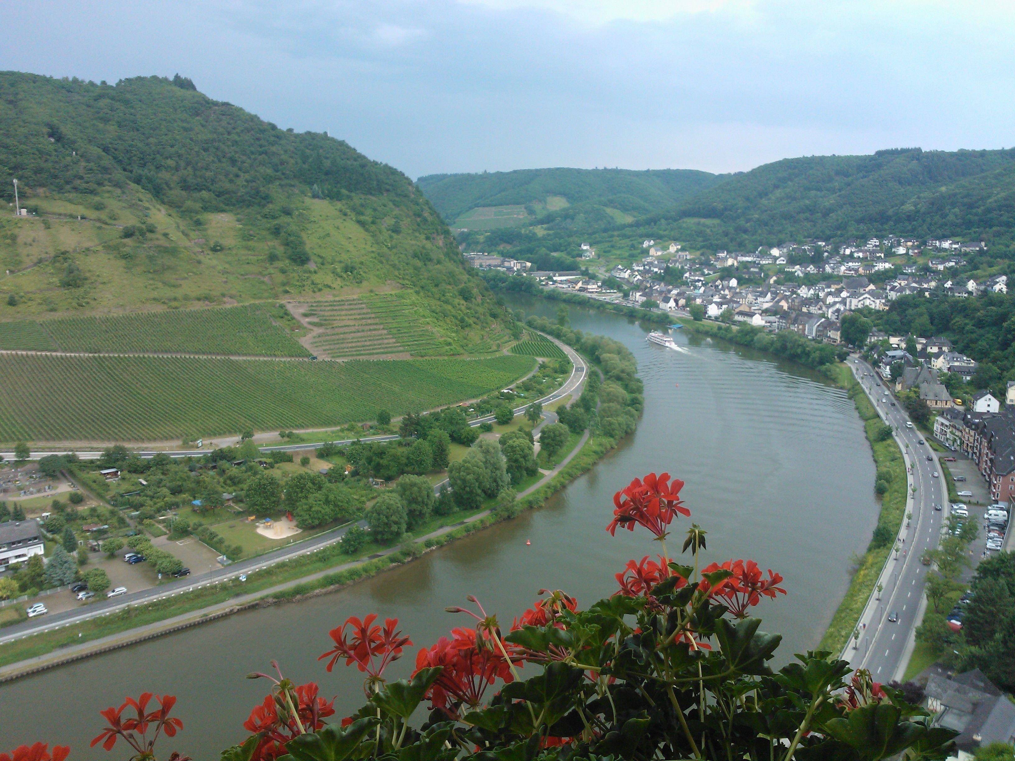 A river flowing through a town with green hills on one side and a bridge crossing the river.