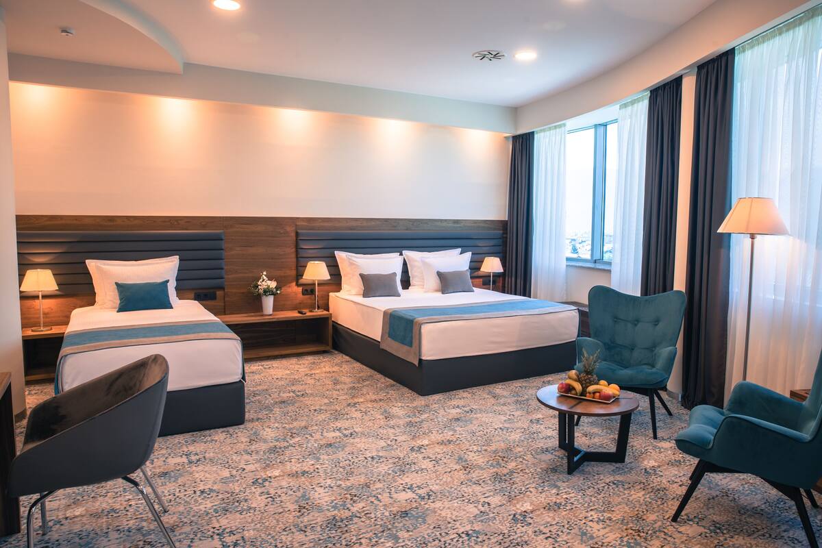 Habitación de hotel con una cama grande, dos mesitas de noche con lámparas, una mesita redonda con fruta y una silla.