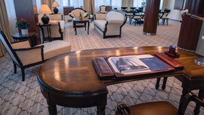 A hotel lobby with a round wooden table, several armchairs, a sofa, and a dining area with a table and chairs. - Radon Plaza (Sarajevo)
