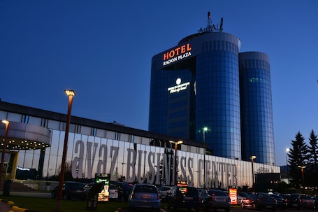A hotel with a modern glass facade, a large sign reading "HOTEL RADON PLAZA," and a visible entrance with a covered area.