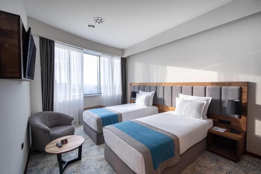 Une chambre d’hôtel avec deux lits, une chaise, une petite table et un téléviseur.