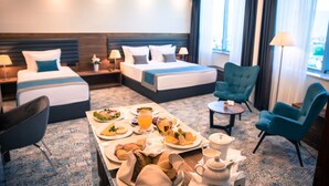 A hotel room with two beds, a dining table with breakfast, a chair, and a lamp. - Radon Plaza (Sarajevo)