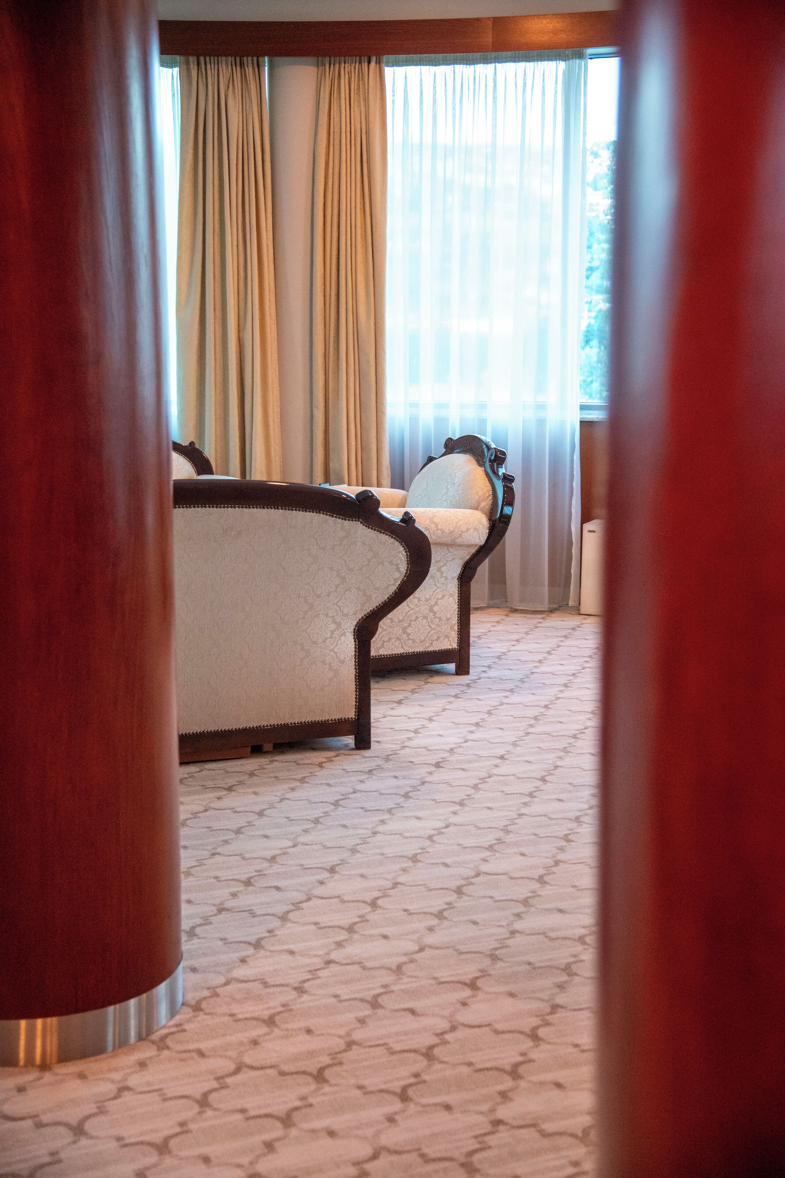A hotel room with a bed, a chair, and a large window with curtains.