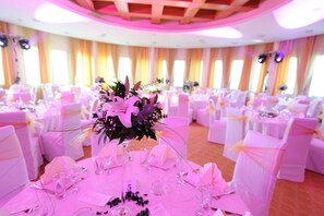 Un salón de banquetes con mesas redondas, sillas blancas y centros de mesa florales.